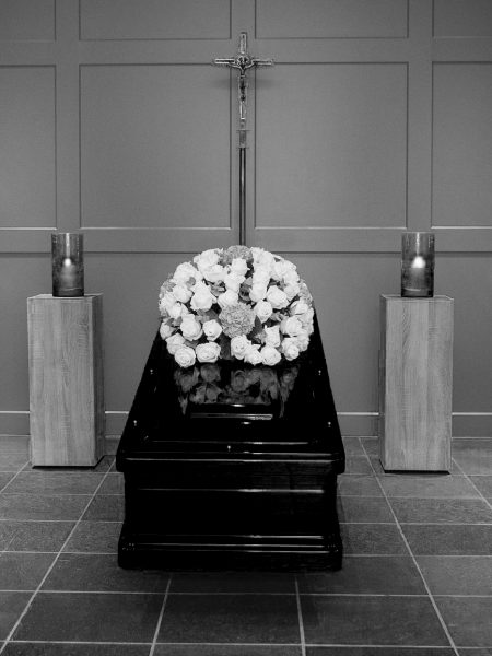 Stijlvolle en Respectvolle Uitvaartkisten voor een Waardig Afscheid Een klassieke houten uitvaartkist met bloemen geplaatst in een serene omgeving.